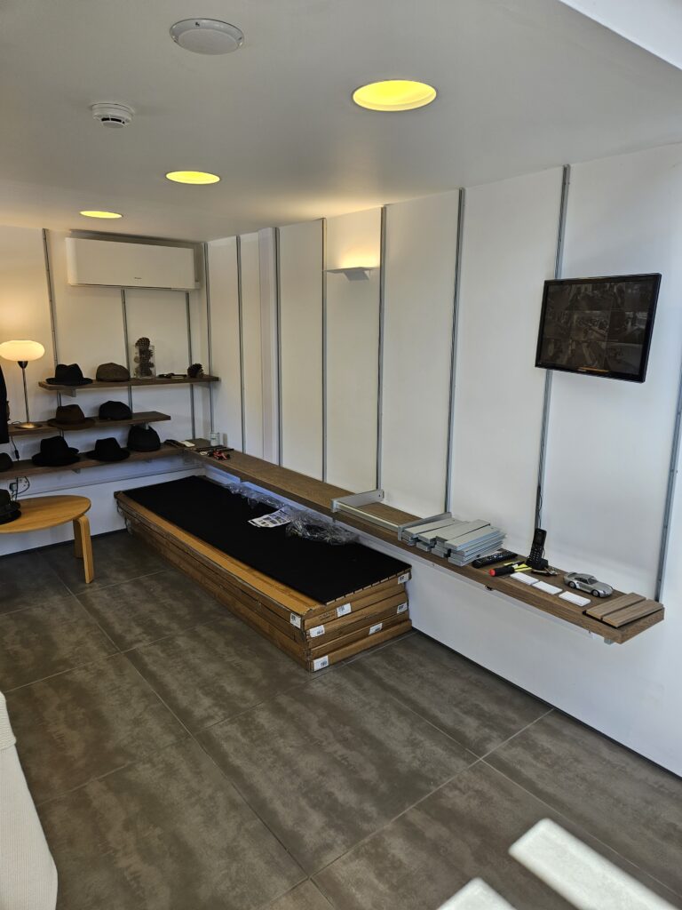 An image of a room with concrete flooring, white walls and shelves with hats on.