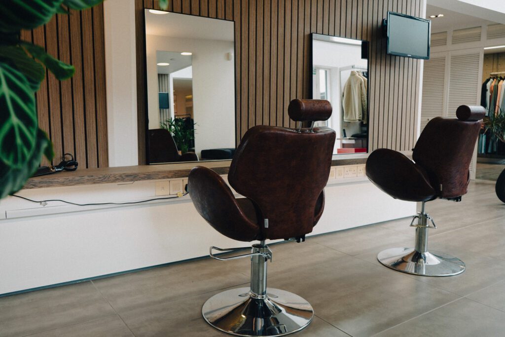 Image of barbershop chairs with mirrors and TV on wall.
