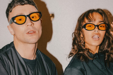 A man and woman wearing sunglasses against a white backdrop.